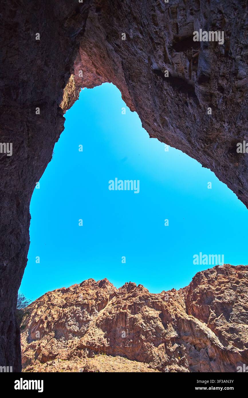 Ouverture de grotte avec des falaises désertiques baignées de soleil et un ciel bleu dans le paysage accidenté de l'Arizona Banque D'Images