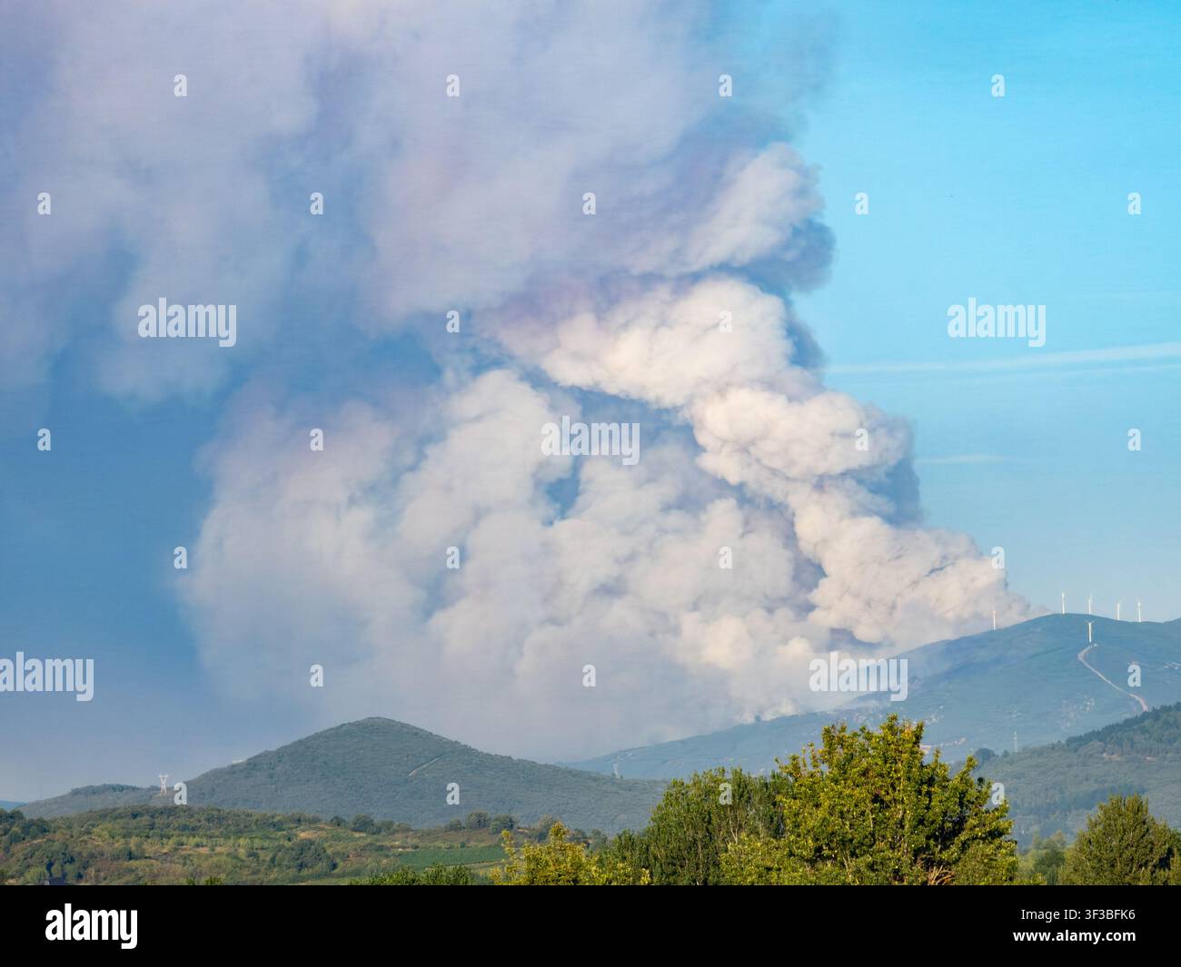 Feu de forêt brûlant dans un paysage montagneux, une énorme colonne de fumée s'élevant dans l'atmosphère claire Banque D'Images