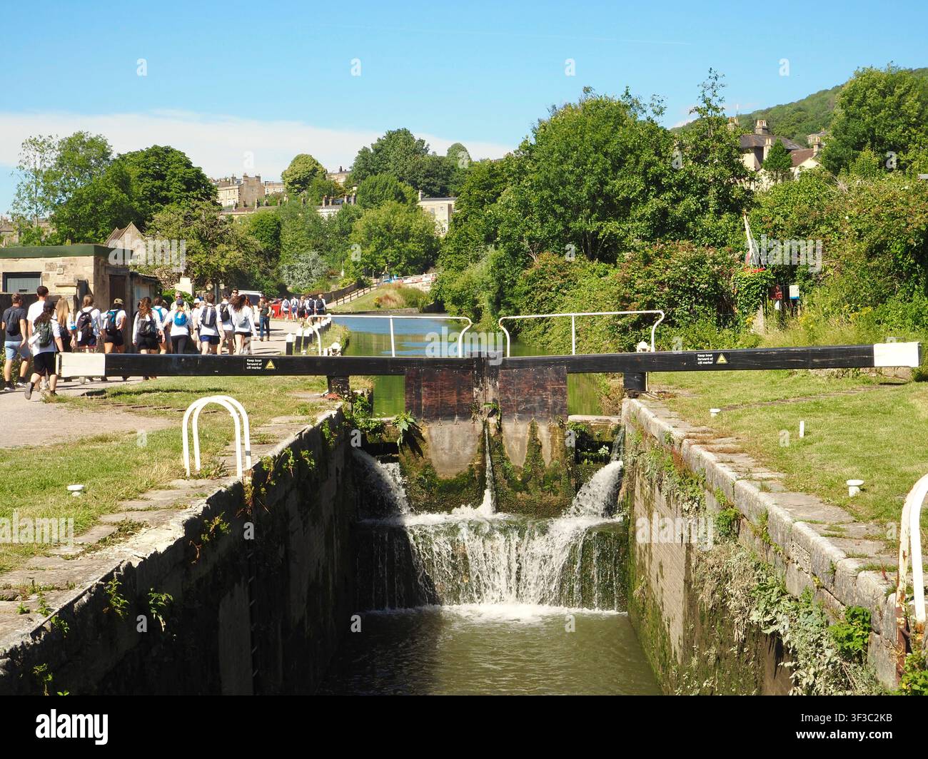 Écluses du canal Kennet et Avon à Widcombe, Bath, Angleterre avec des promeneurs ou des randonneurs sur le chemin de halage et des plantes poussant sur les écluses en bois Banque D'Images