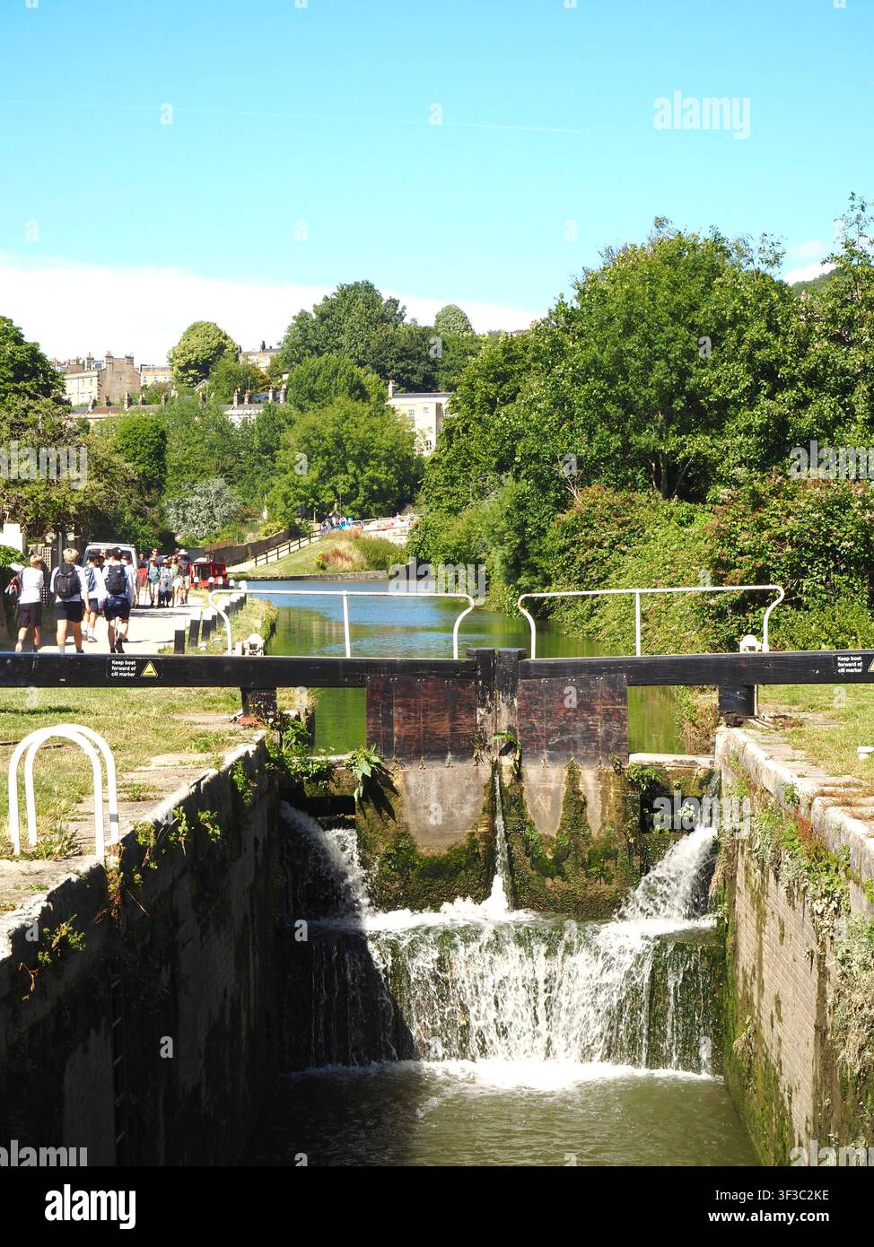 Écluses du canal Kennet et Avon à Widcombe, Bath, Angleterre avec des promeneurs ou des randonneurs sur le chemin de halage et des plantes poussant sur les écluses en bois Banque D'Images