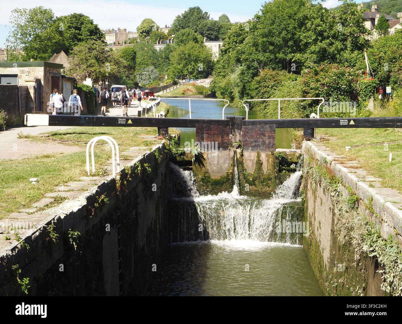 Écluses du canal Kennet et Avon à Widcombe, Bath, Angleterre avec des promeneurs ou des randonneurs sur le chemin de halage et des plantes poussant sur les écluses en bois Banque D'Images