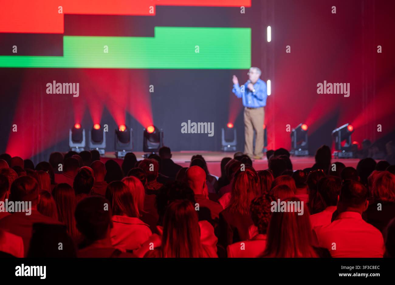 Conférencier interagissant avec le public dans une salle de conférence éclairée par des lumières rouges et bleues. Banque D'Images