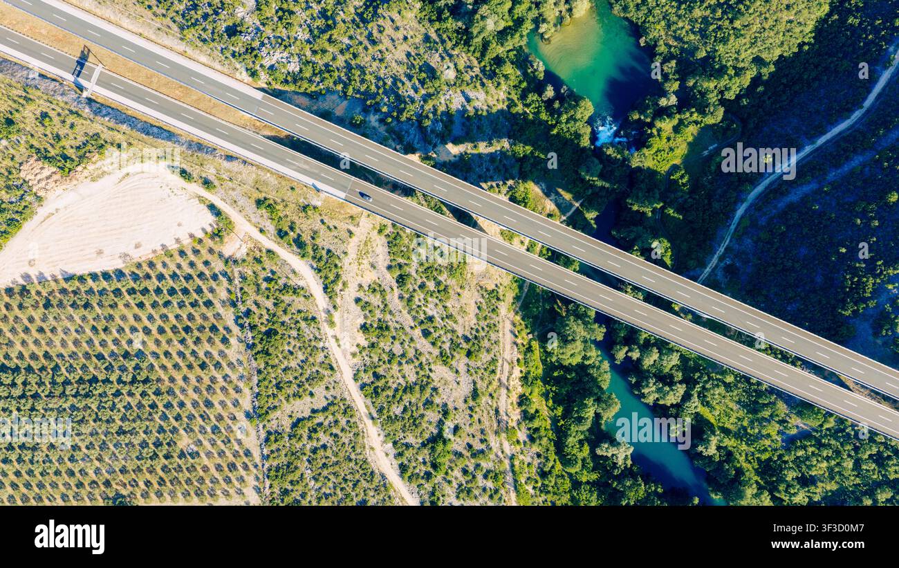 Vue aérienne par le dessus d'un pont d'autoroute moderne traversant une rivière émeraude à travers une vallée verte Banque D'Images