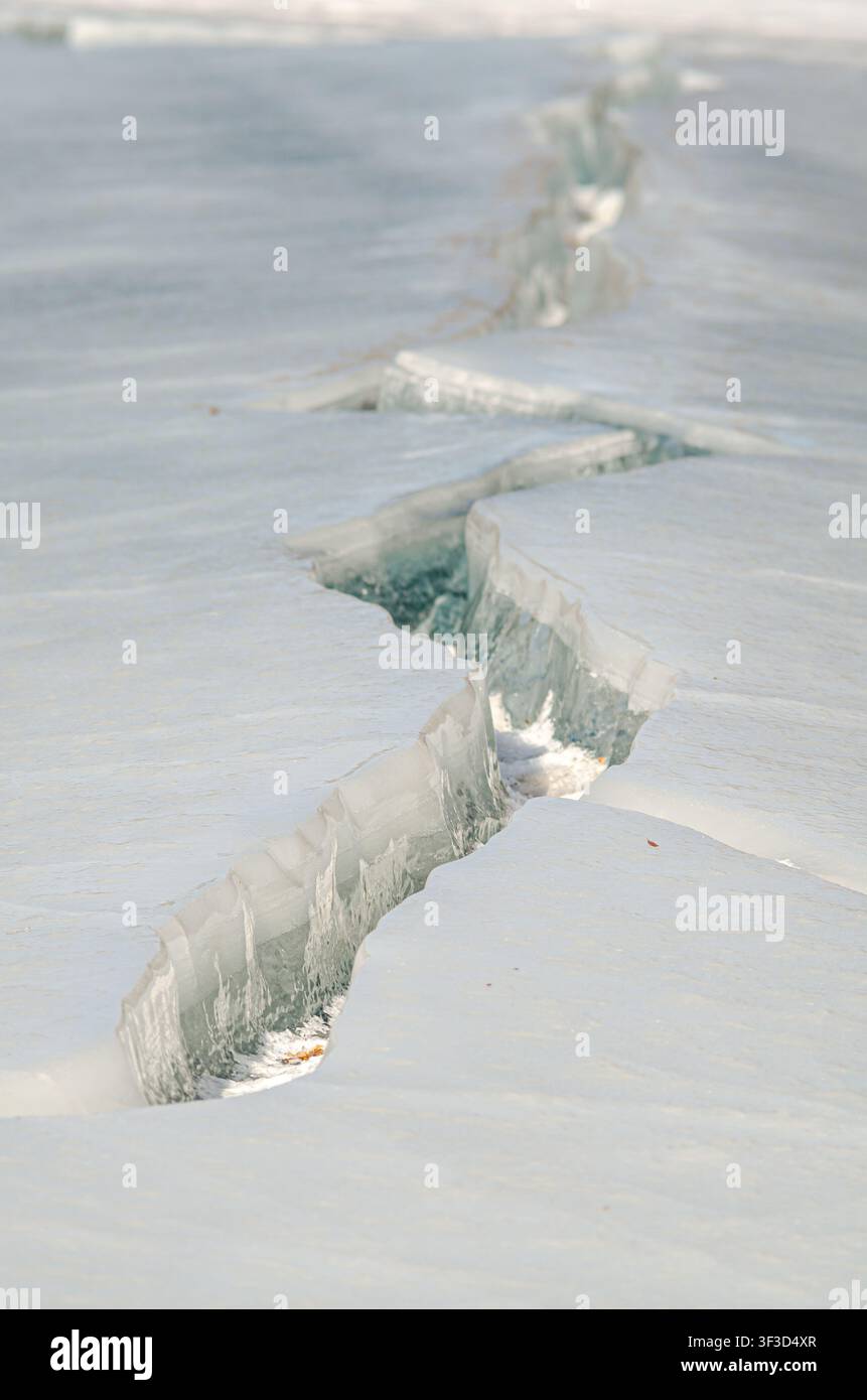 Gros plan vertical d'une fissure dans la glace d'une rivière gelée, montrant une fissure naturelle dans la glace, une texture hivernale et un fond froid abstrait avec espace de copie Banque D'Images