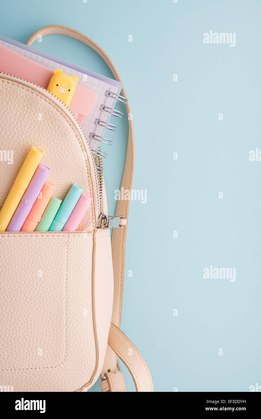 Ouverture du sac à dos révélant des cahiers à spirale et un charmant effaceur en forme de cochon, avec une poche avant contenant une collection de marqueurs pastel colorés, tout Banque D'Images