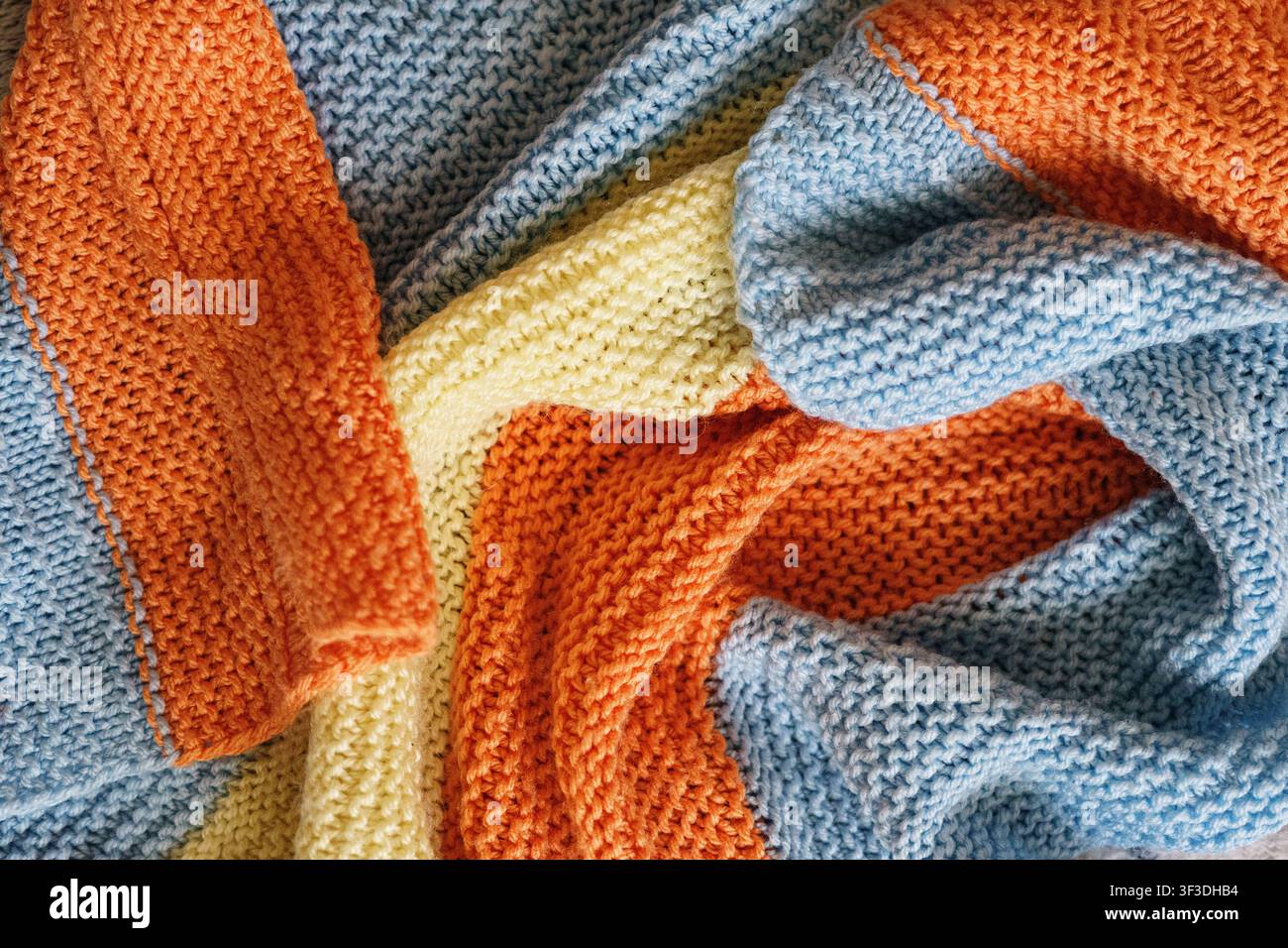 Couverture tricotée douce dans des tons bleu pastel, crème et orange. Fond en tissu texturé confortable avec une atmosphère chaleureuse à la maison. Banque D'Images