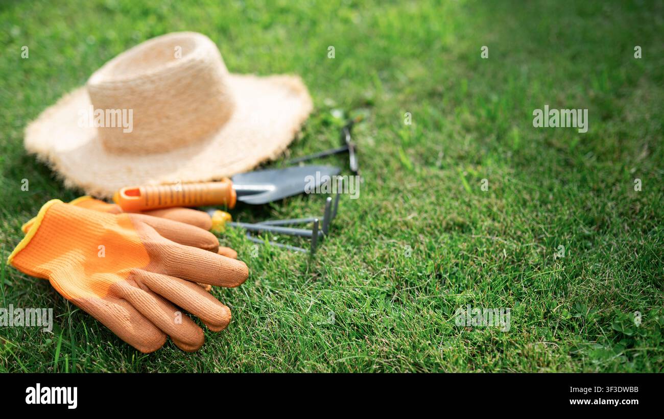 Gants de jardinage, chapeau de paille et outils à main disposés sur de l'herbe verte fraîche. Équipement de jardinage pour la plantation au printemps et les travaux de cour en plein air. Copie Banque D'Images