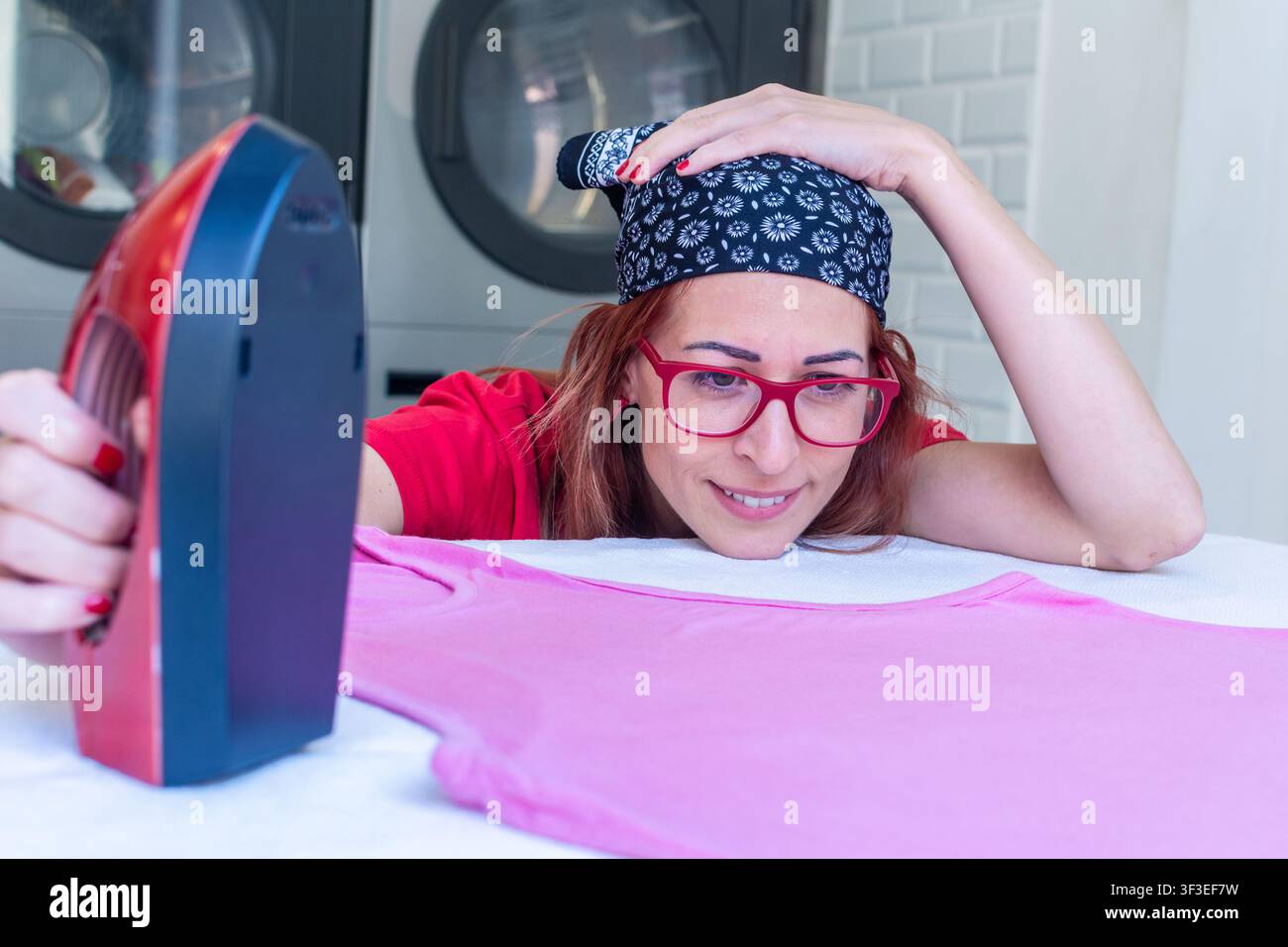 Femme repassant une chemise rose dans une buanderie Banque D'Images