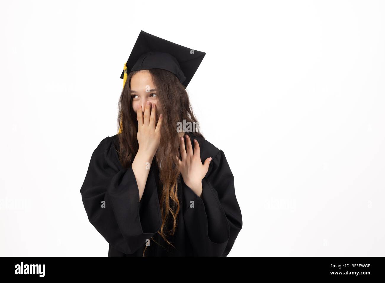 Jeune diplômée portant une coiffe académique ajustant son manteau et tenant son diplôme Banque D'Images