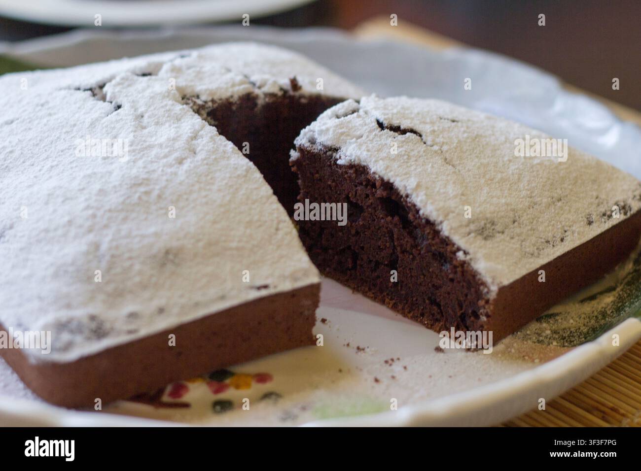 Close-up d'un gâteau au chocolat fait maison saupoudré de sucre glace et coupé pour montrer la mie sombre et moelleuse sur une assiette en céramique peinte à la main Banque D'Images