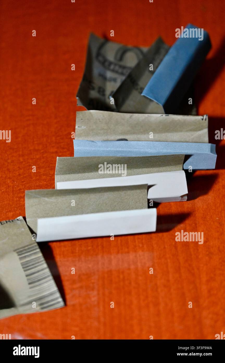 Photographie en gros plan de bandes de papier abrasif étanches pliées et de blocs de ponçage en caoutchouc disposés sur un établi en bois orange. Outils et équipements abrasifs essentiels utilisés par les luthiers pour le nivellement des frettes, le polissage, le ponçage du bois et la restauration d'instruments. Banque D'Images
