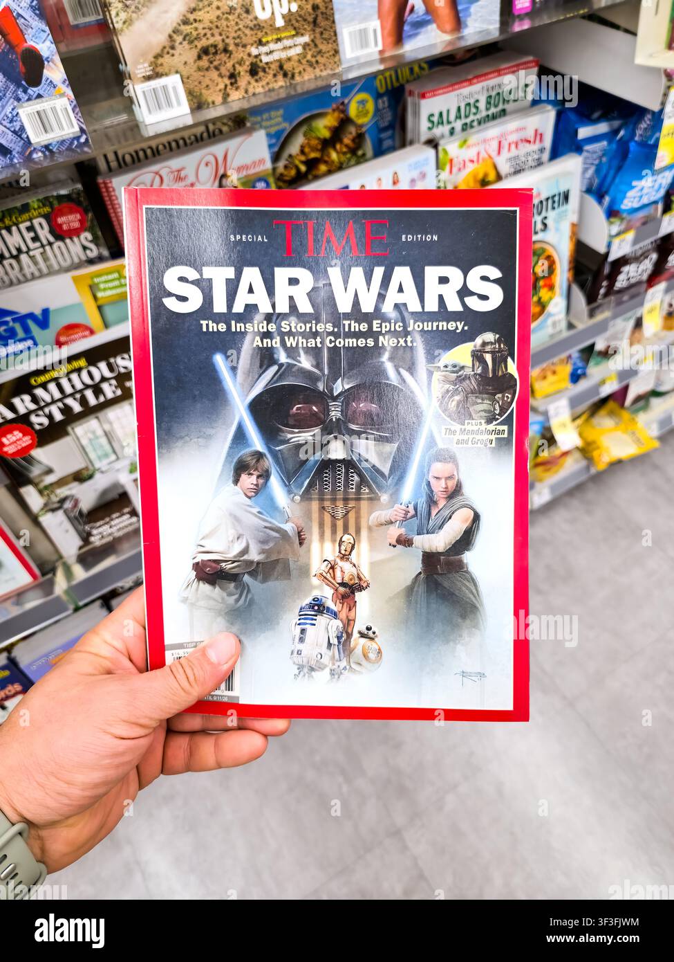 DALLAS, TX, USA - 19 JUILLET 2026 : Une personne tient une édition spéciale du Time Magazine mettant en vedette Star Wars, exposée sur une étagère de magasin avec divers autres produits Banque D'Images