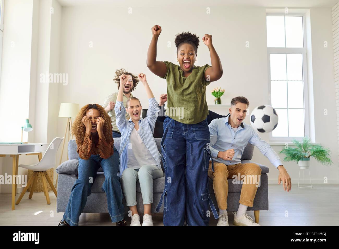Des amis applaudissent un but de football à la maison, célébrant en regardant à la télévision Banque D'Images