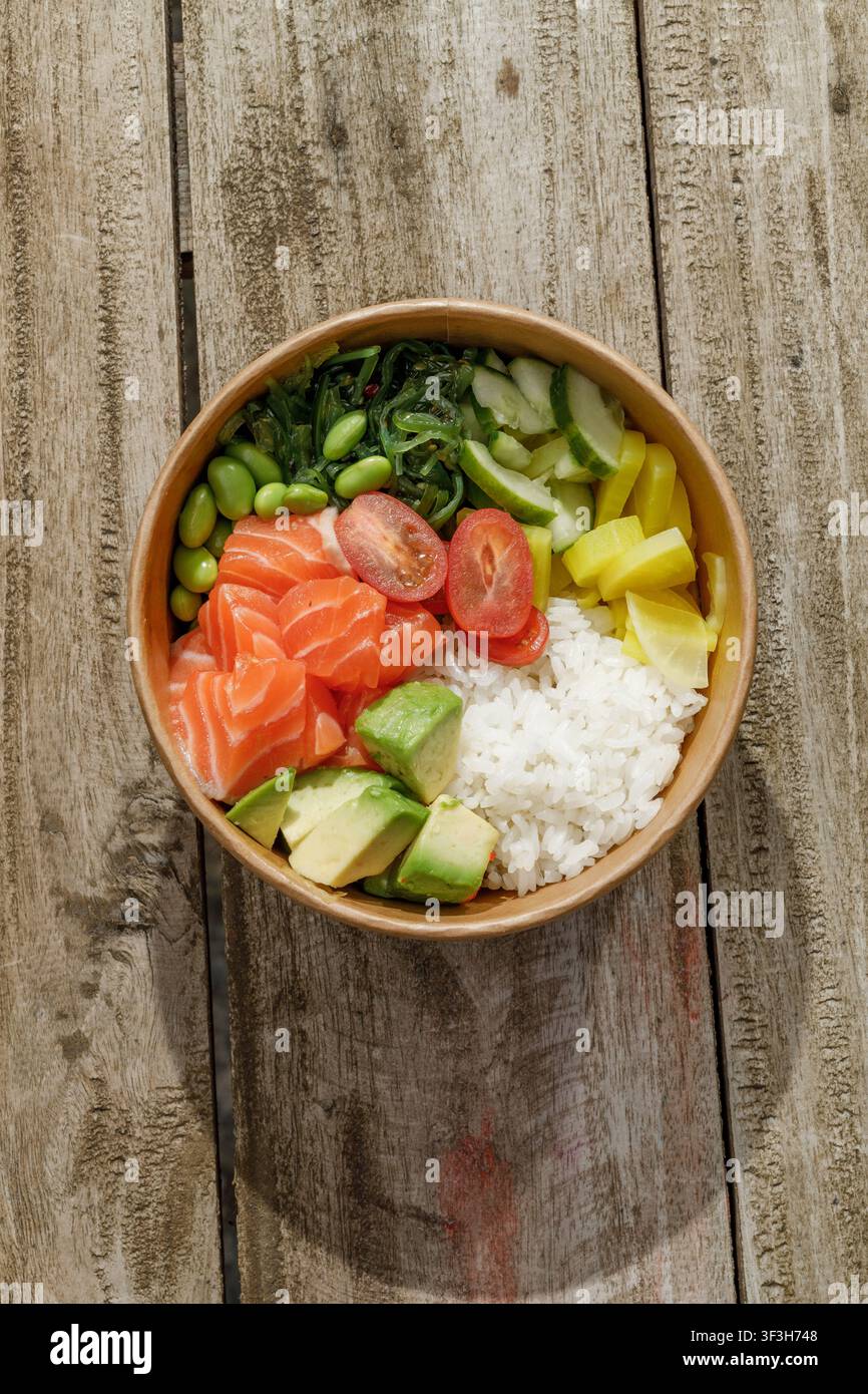 Bol poke au saumon dans une boîte de livraison sur une surface en bois. Isolé Banque D'Images