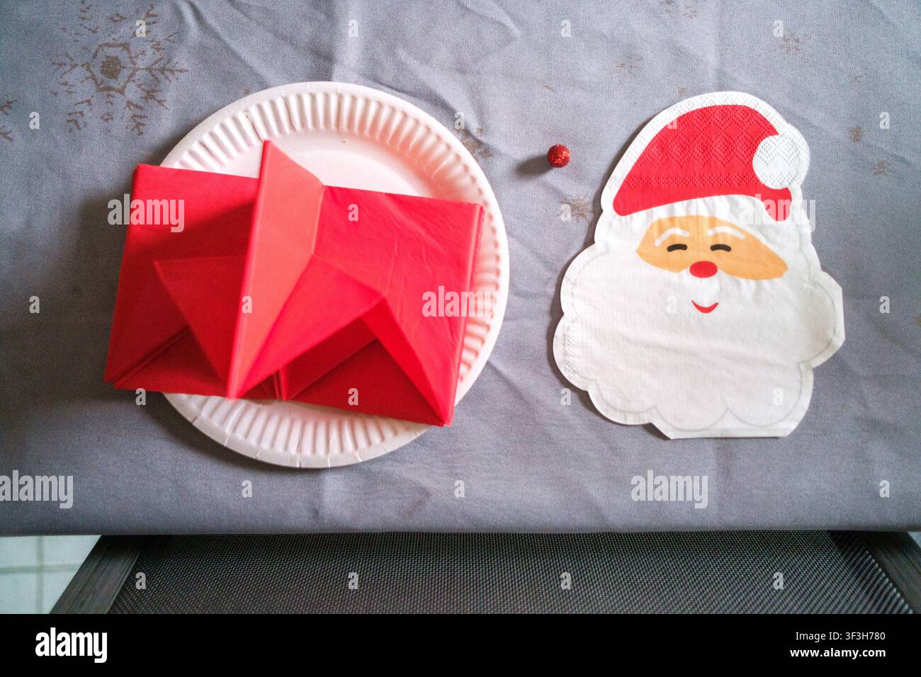 Vue aérienne d'un objet de Noël en papier fait à la main rouge sur une assiette en carton à côté d'une serviette du Père Noël et d'un petit ornement rouge sur une table dans une maison familiale Banque D'Images