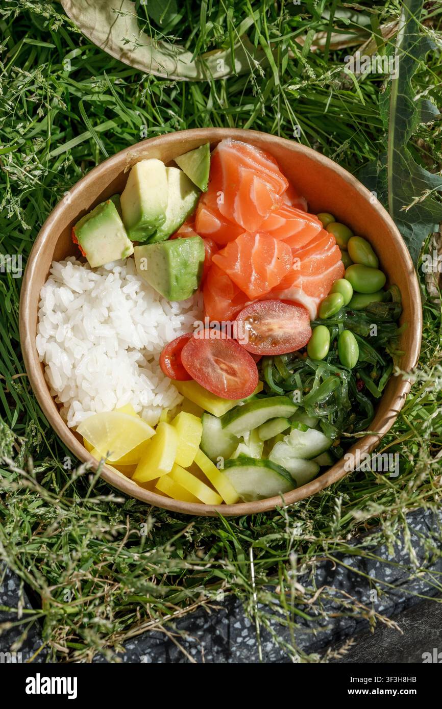Bol poke au saumon dans une boîte de livraison sur de l'herbe verte. Banque D'Images