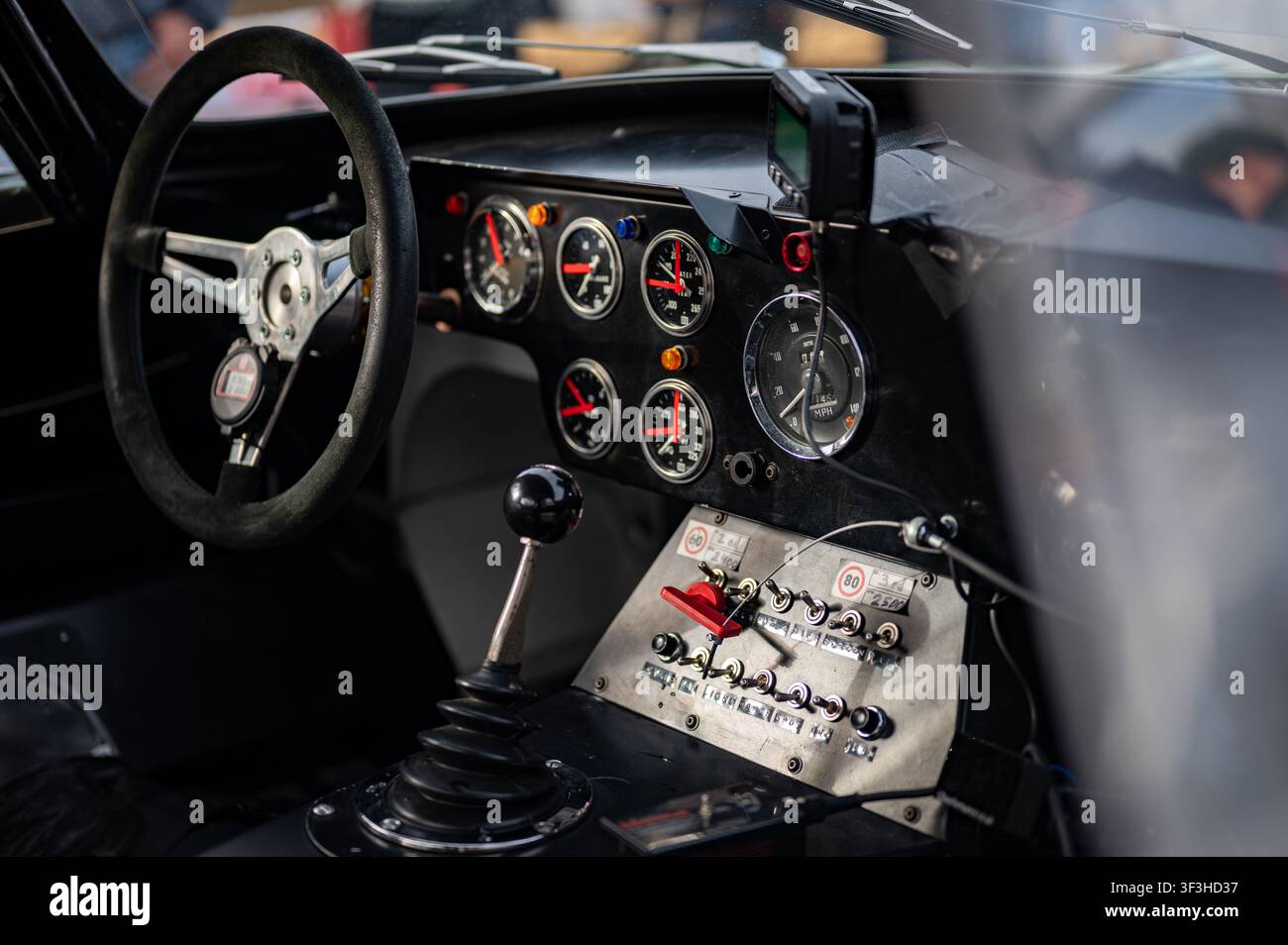Vue détaillée de l'intérieur d'une voiture de course classique sur mesure présentant un tableau de bord avec des jauges analogiques, un panneau à interrupteurs à bascule et une manuelle de vitesse. Banque D'Images