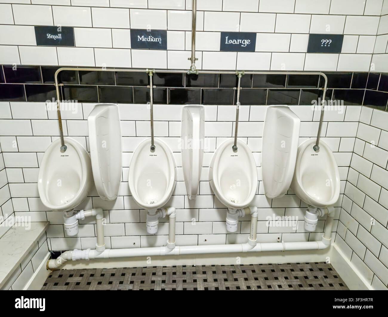 Panneaux amusants au-dessus des urinoirs dans les toilettes pour hommes avec des inscriptions indiquant 'petit', 'moyen', 'grand' et '???', Angleterre, Royaume-Uni - Image de stock capturée avec un smartphone