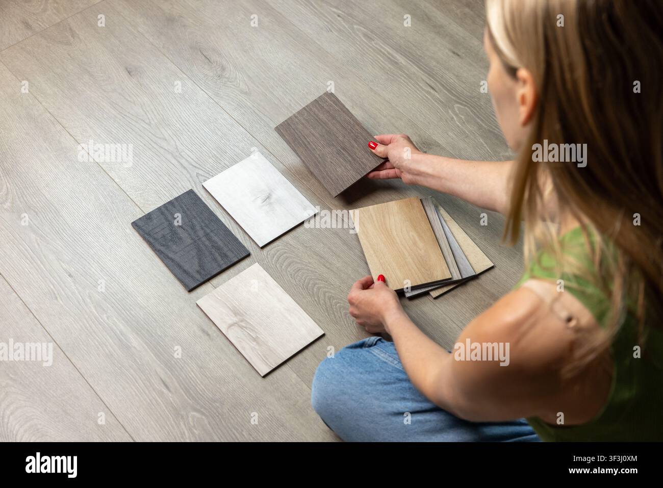 Femme assise par terre et choisissant des échantillons de parquet pour la rénovation de la maison et la décoration intérieure Banque D'Images