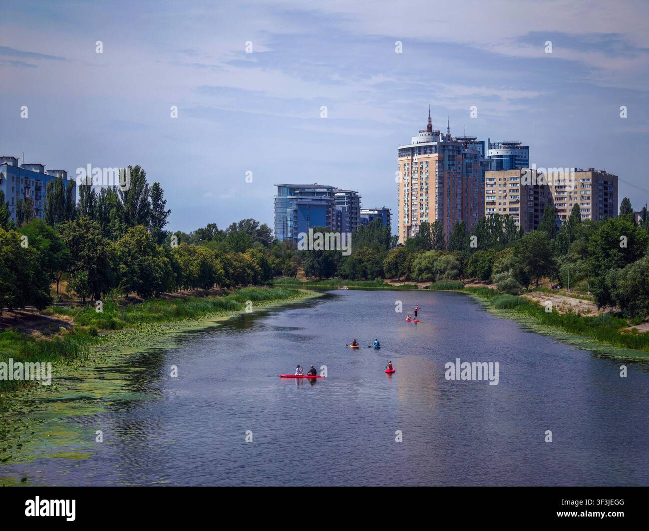 Des gens profitant d'activités de loisir comme le kayak et le stand up paddle sur le canal de Rusanivka, entourés d'arbres verts et d'immeubles d'appartements modernes Banque D'Images