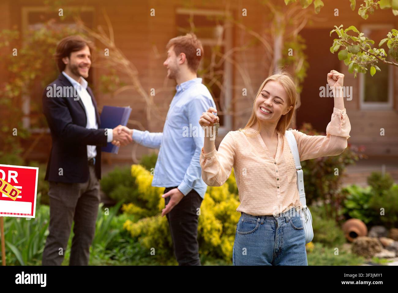 Bonne jeune femme avec la clé de la maison et son mari secouant mains avec le realtor dans l'arrière-cour Banque D'Images