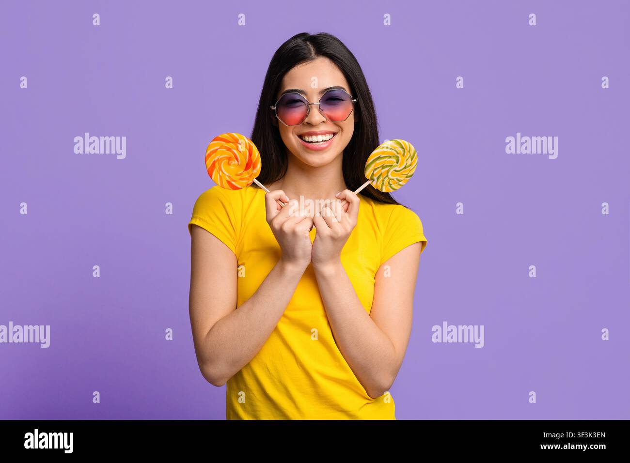 Douceur. Jolie jeune femme d'été couvrant l'oeil avec grand lulllipop lumineux et regardant la caméra, fond jaune avec espace de copie Banque D'Images