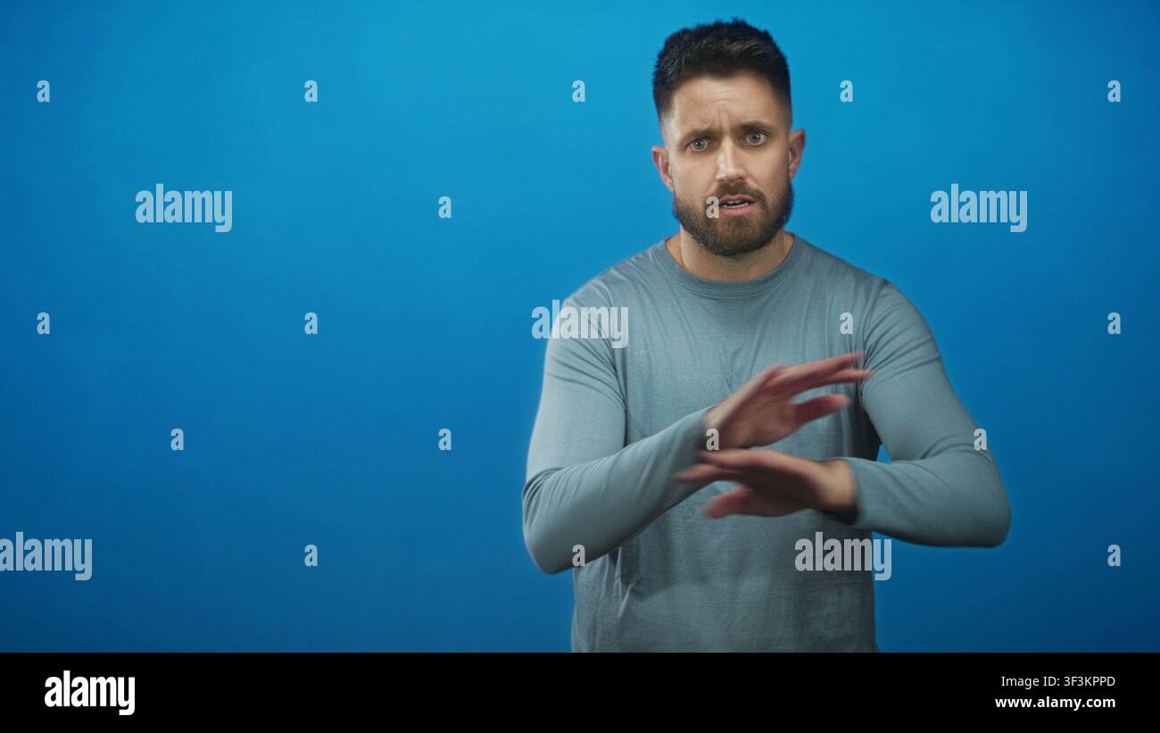 Homme à la barbe et aux mains visibles haussant les paumes vers le haut et levant les sourcils sur un fond de studio bleu sans couture ; incertitude. Banque D'Images