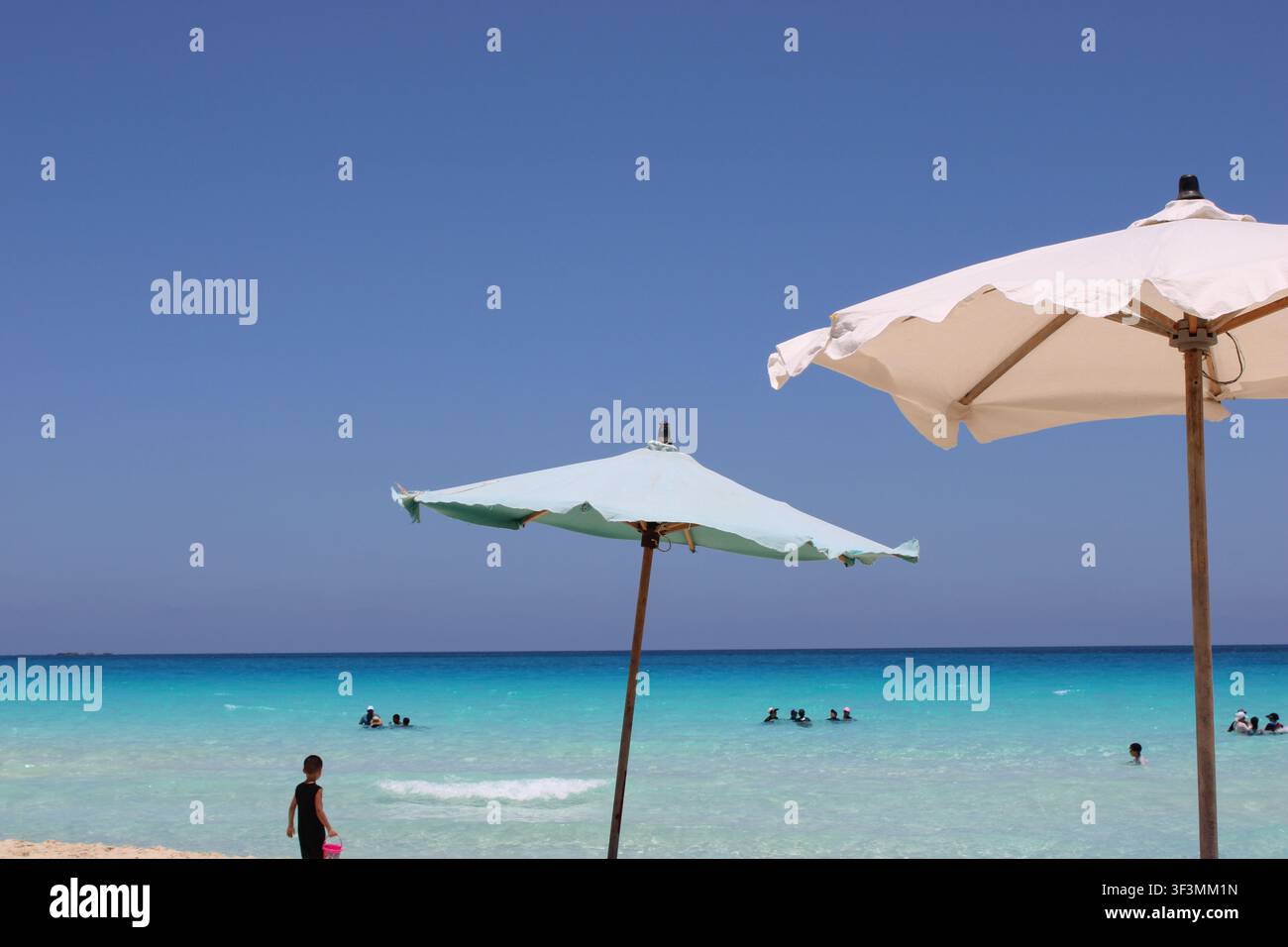 Les eaux turquoise cristallines de White Beach à Marsa Matrouh créent l’une des destinations estivales les plus époustouflantes d’Égypte, où des parasols blancs, Banque D'Images