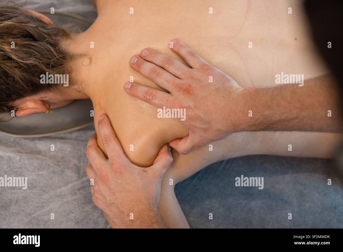 Mains d'un physiothérapeute massant le haut du dos du patient pendant une séance de thérapie Banque D'Images