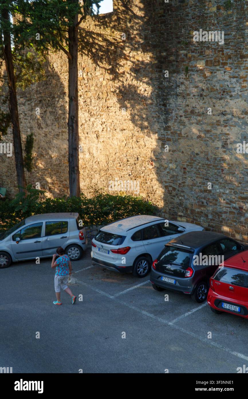 Florence, Toscane, Italie. 28 mai 2026. - Une femme marche à travers un parking goudronné sous de grands arbres et un ancien mur de pierre pendant la dorée Banque D'Images