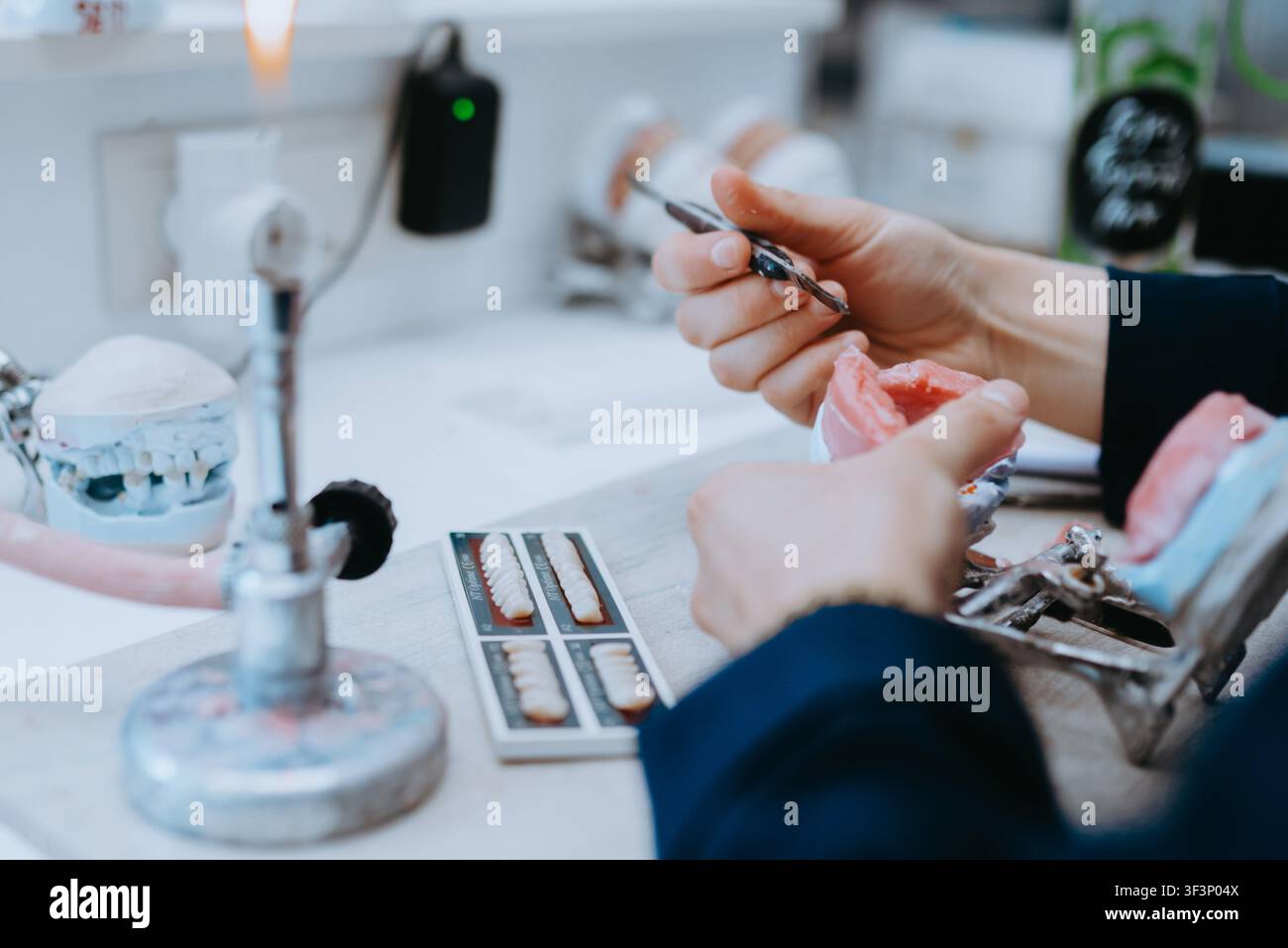Technicien dentaire fabriquant des prothèses dans un laboratoire avec un guide de teinte dentaire et un moule dentaire Banque D'Images