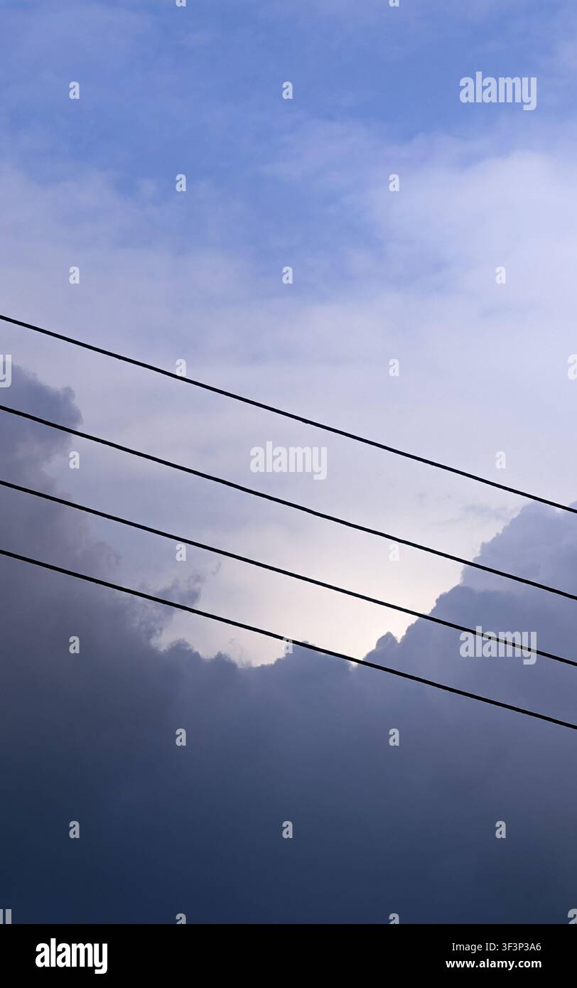 Vue minimaliste de lignes électriques se détachant sur un ciel bleu dramatique et des nuages d'orage Banque D'Images