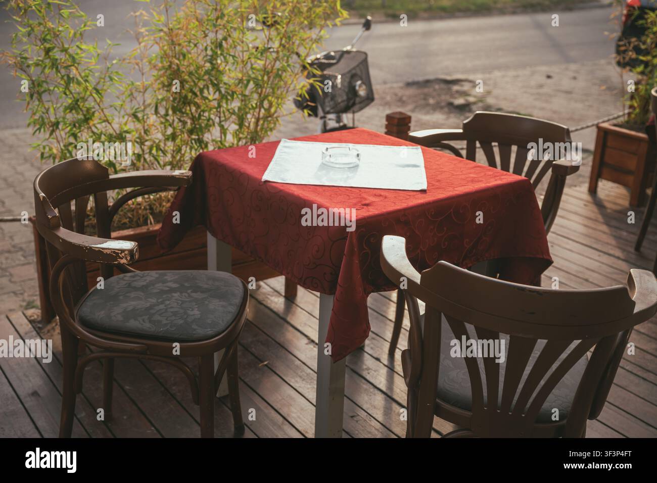 Prise de vue en hauteur d'une table de café extérieure vide dressée avec une nappe rouge, un chemin de table blanc, un cendrier et trois chaises en bois. Mise au point sélective. Banque D'Images