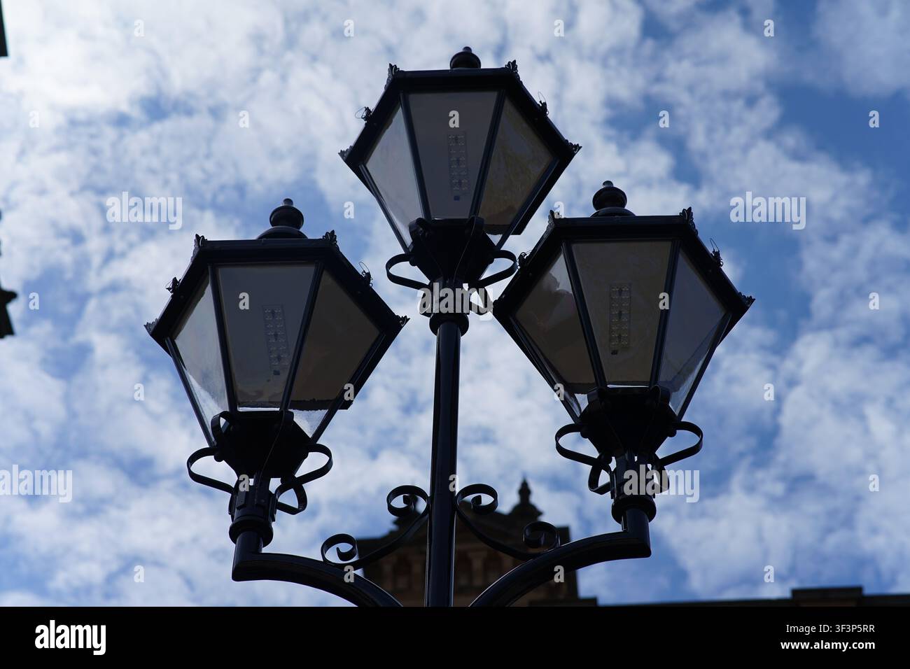 Un lampadaire antique en métal noir orné de lanternes vintage contre un ciel bleu clair de jour. Banque D'Images