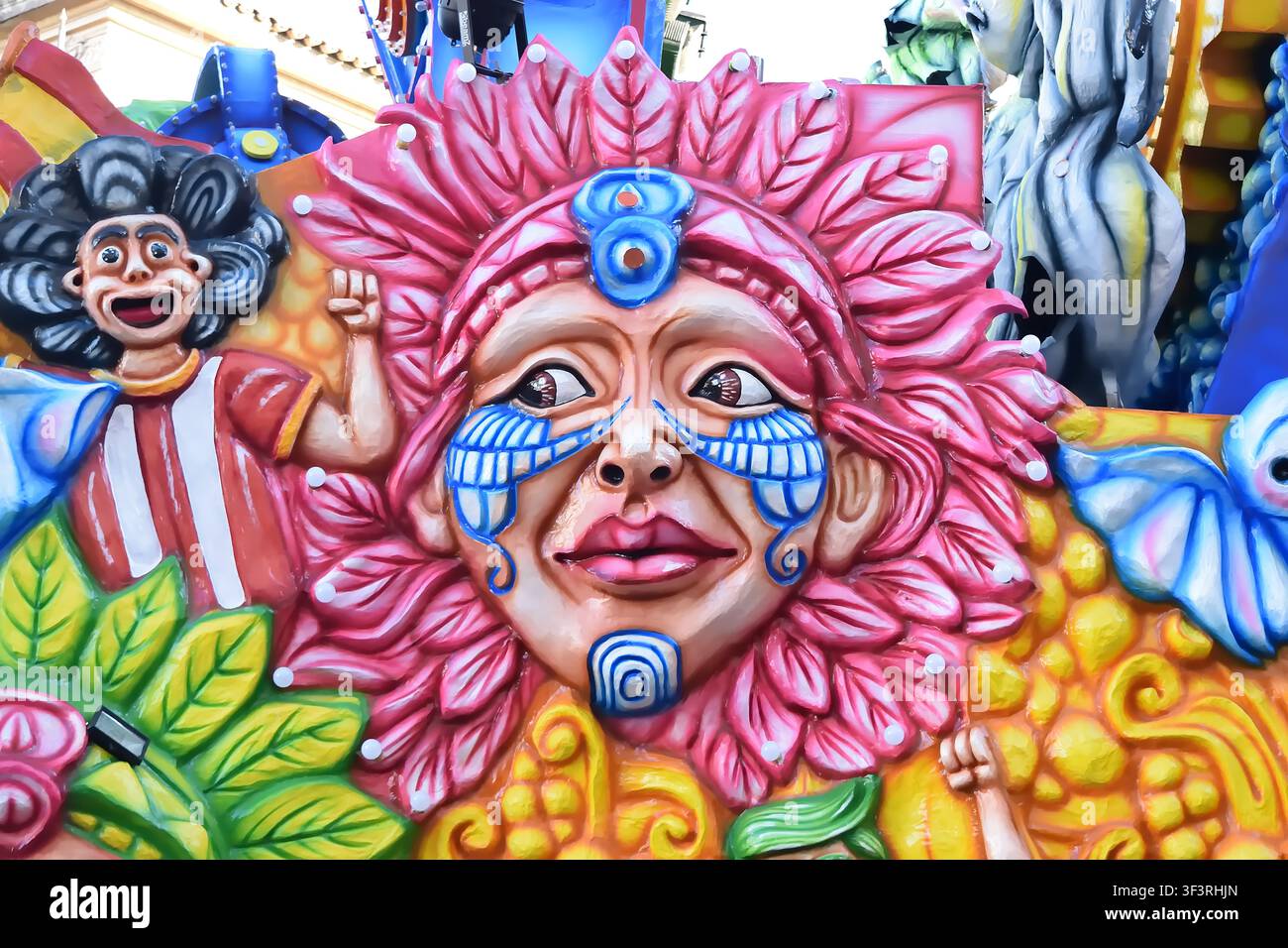 Acireale (CT), Italie - 22 février 2026 : char allégorique représentant un visage floral avec une peinture tribale bleue et des pétales rose vif pendant le carnaval Banque D'Images
