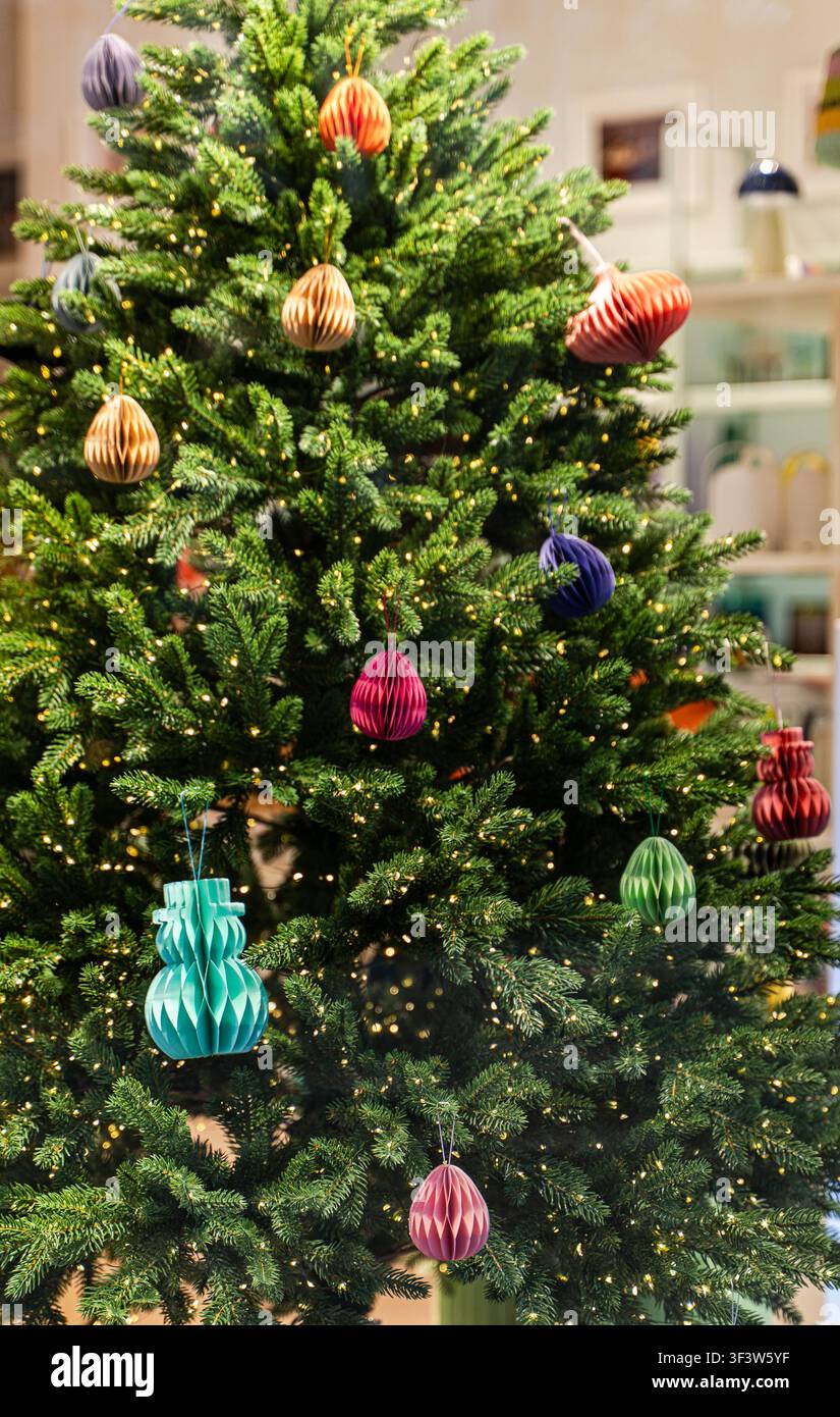 Sapin de Noël intérieur décoré d'ornements en boules en papier coloré et de lumières chaudes de guirlande, créant une scène de décoration d'intérieur festive et chaleureuse avec un doux bo Banque D'Images