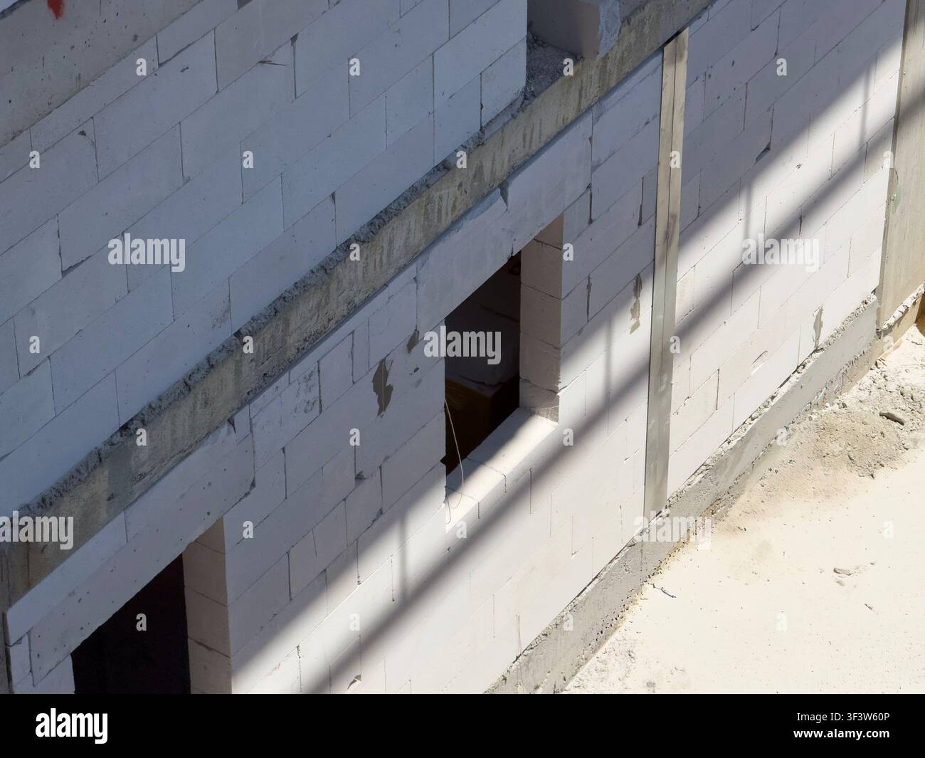 Close-up d'un mur inachevé en blocs de béton alvéolaire blanc avec des joints de mortier rugueux et des ouvertures de fenêtres, capturé au soleil sur un bâtiment Banque D'Images