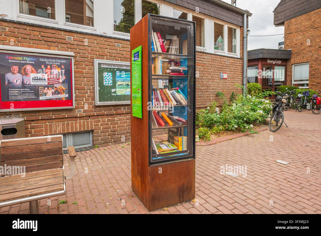 Bibliothèque extérieure publique pour le bookcrossing sur une rue européenne avec des bâtiments en briques, des panneaux d'affichage et un banc en bois par une journée nuageuse Banque D'Images