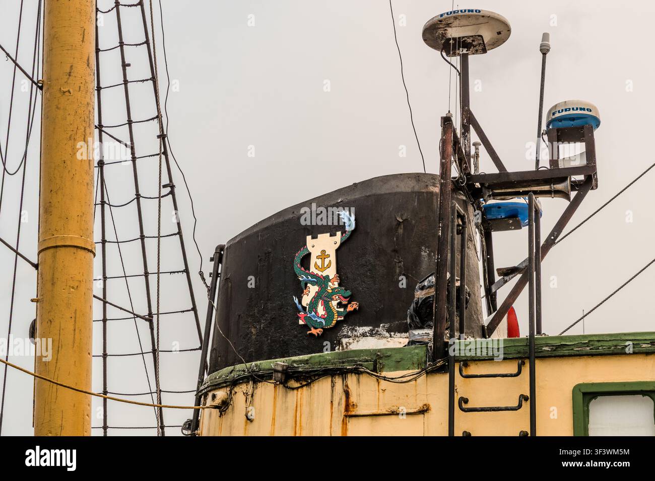 Un blason en bois représentant un dragon stylisé et une ancre orne la cheminée du Picton Castle à Lunenburg, en Nouvelle-Écosse, sous les antennes de navigation modernes Furuno. Le contraste entre l’ornementation traditionnelle et la technologie moderne de radio et de radar illustre comment le navire d’entraînement à la navigation, construit en 1928, est équipé pour ses voyages d’entraînement. Lunenburg, Nouvelle-Écosse, Canada Banque D'Images