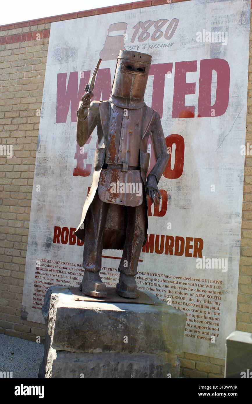 Une statue en métal patinée de Ned Kelly tenant un pistolet, placée devant une affiche vintage de 1880 recherchée à Glenrowan, Victoria, Australie Banque D'Images