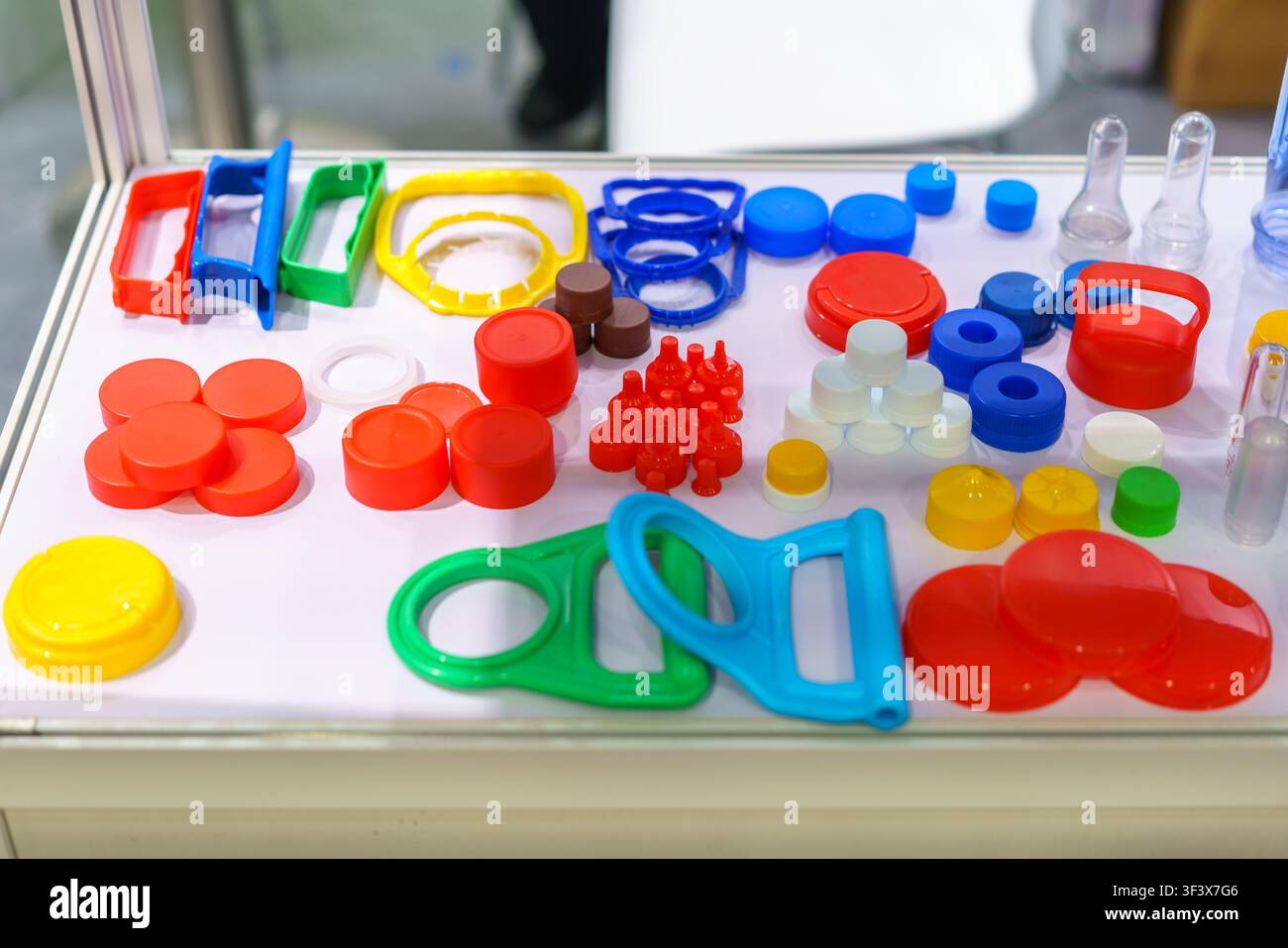 Gros plan de divers bouchons, couvercles et poignées de transport colorés en plastique disposés sur une table blanche lors d'une exposition de fabrication d'emballages. Banque D'Images