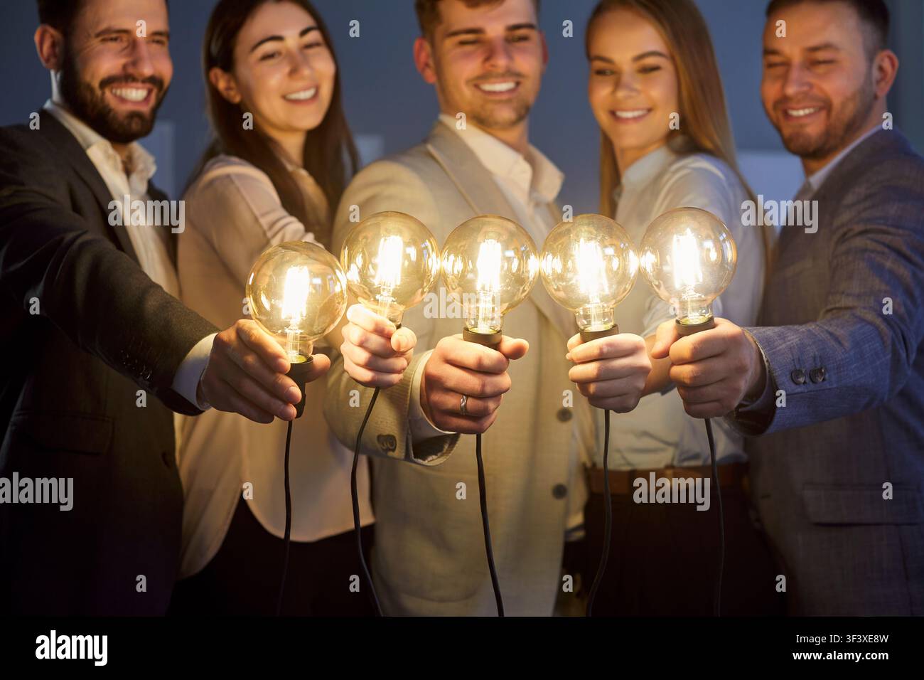 Groupe de professionnels souriants et heureux debout en rangée tenant et reliant des ampoules à l'intérieur. Banque D'Images