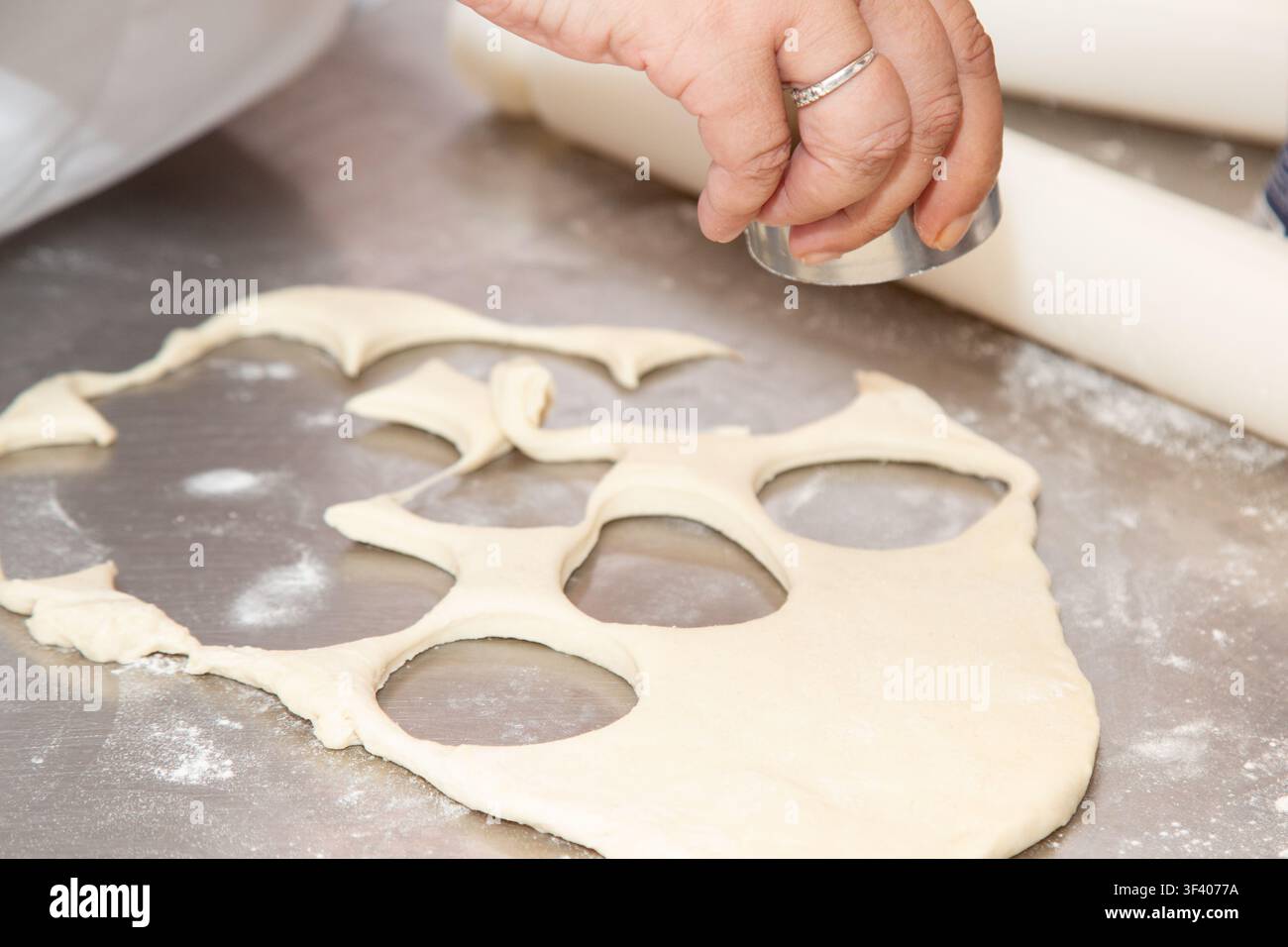 Main façonnant une pâte roulée avec un emporte-pièce métallique sur un plan de travail en acier inoxydable fariné, créant des découpes circulaires pour la préparation de pâtisseries maison Banque D'Images
