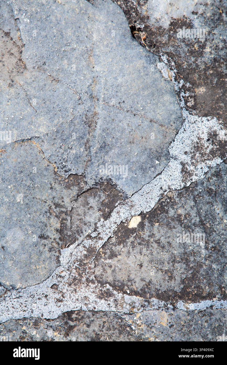 Surface en pierre grise érodée avec des fissures, une texture minérale rugueuse, des veines pâles, des taches sombres et des bords usés formant un fond naturel abstrait pour Banque D'Images