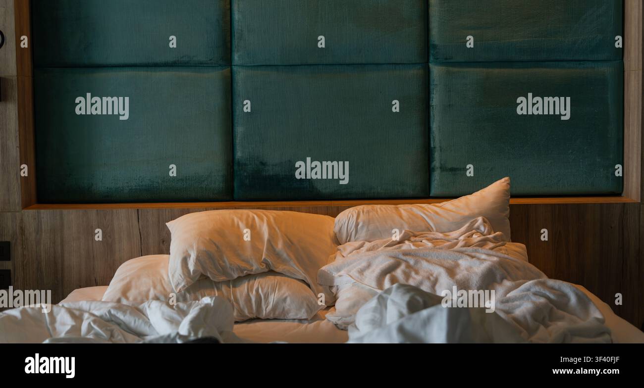 Lit défait désordonné avec des oreillers blancs et une couverture froissée dans la chambre. Banque D'Images