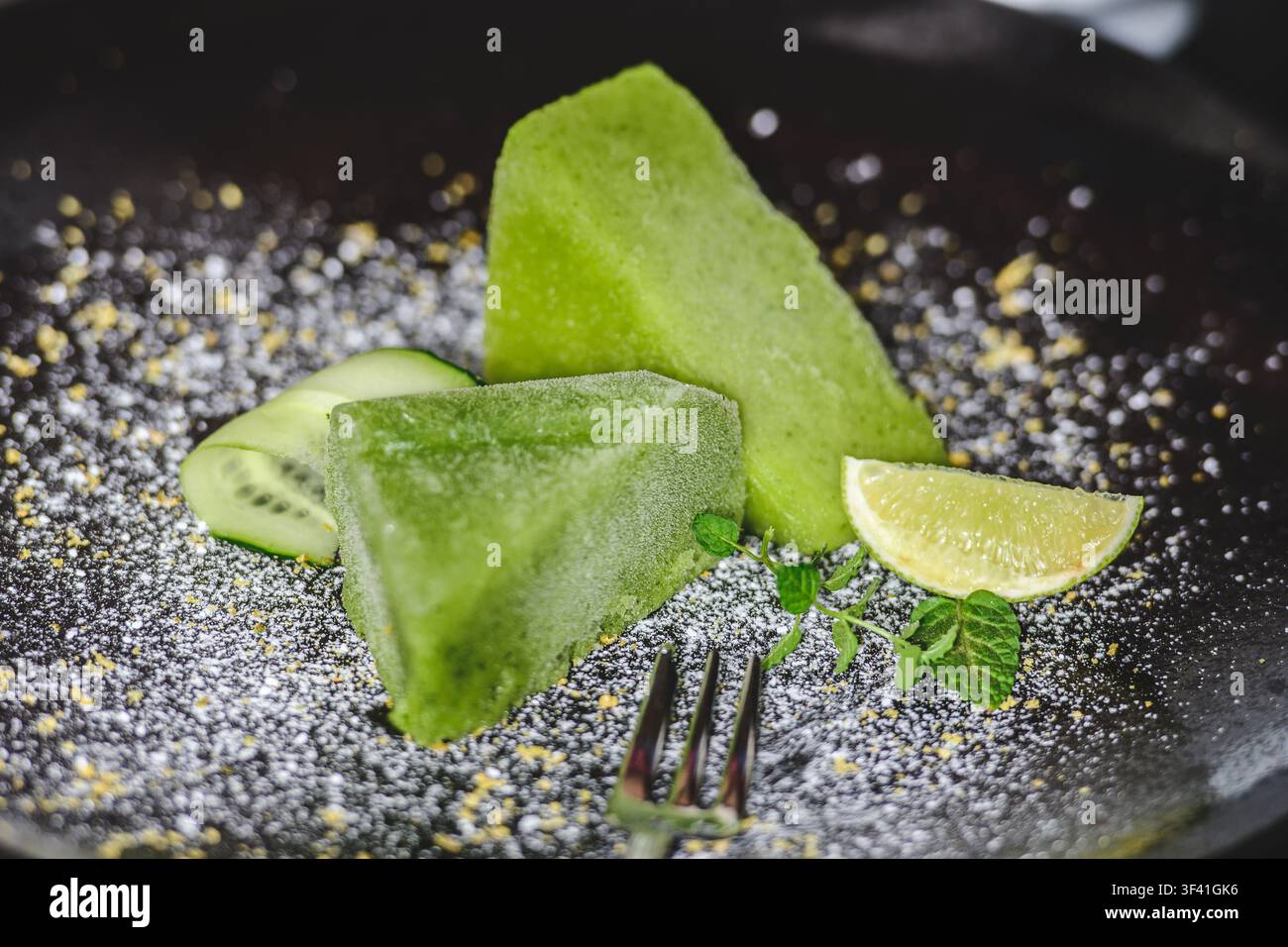 Sorbet vert à la concombre mixée, accompagné de tranches de concombre fraîches, d'un quartier de lime, de brins de menthe et d'une légère poussière de poudre ou de zeste Banque D'Images