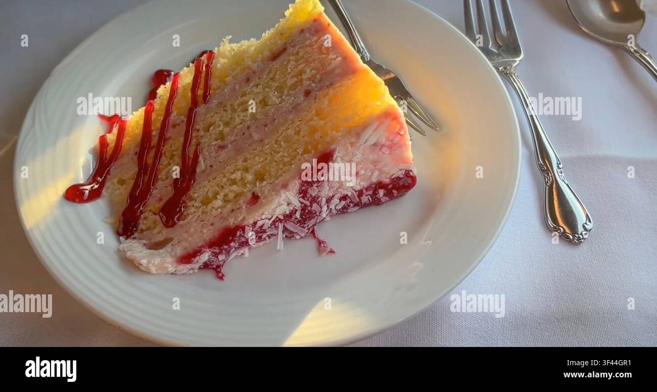 Une part de gâteau aux couches de framboises garnie d'un glaçage à la crème et d'une coulée de baies rouges, servie avec une fourchette sur une nappe blanche. Gros plan sur la nourriture Banque D'Images