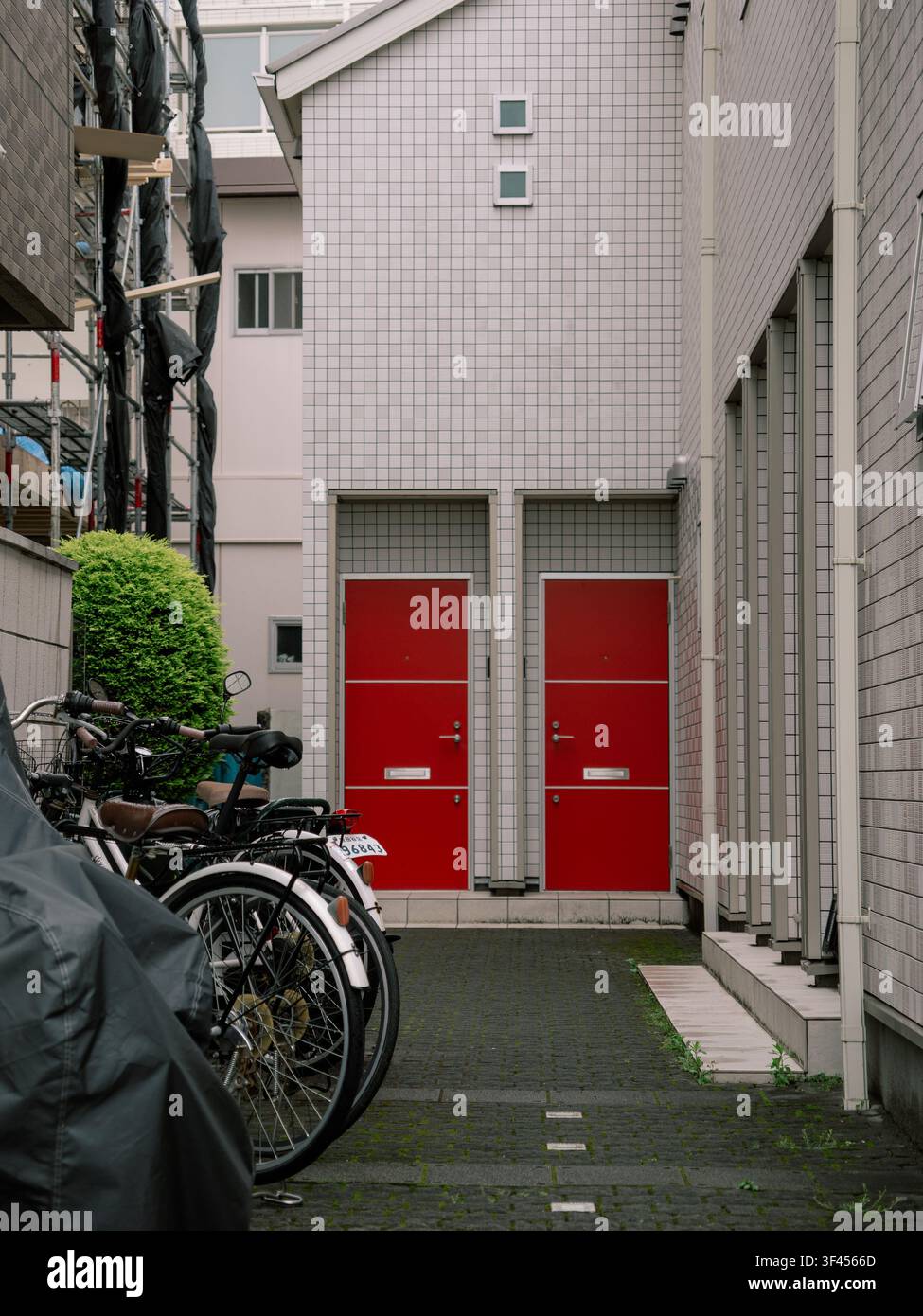 Deux portes d'entrée rouges d'un immeuble d'appartements résidentiels avec des vélos garés dans une ruelle étroite, Japon Banque D'Images