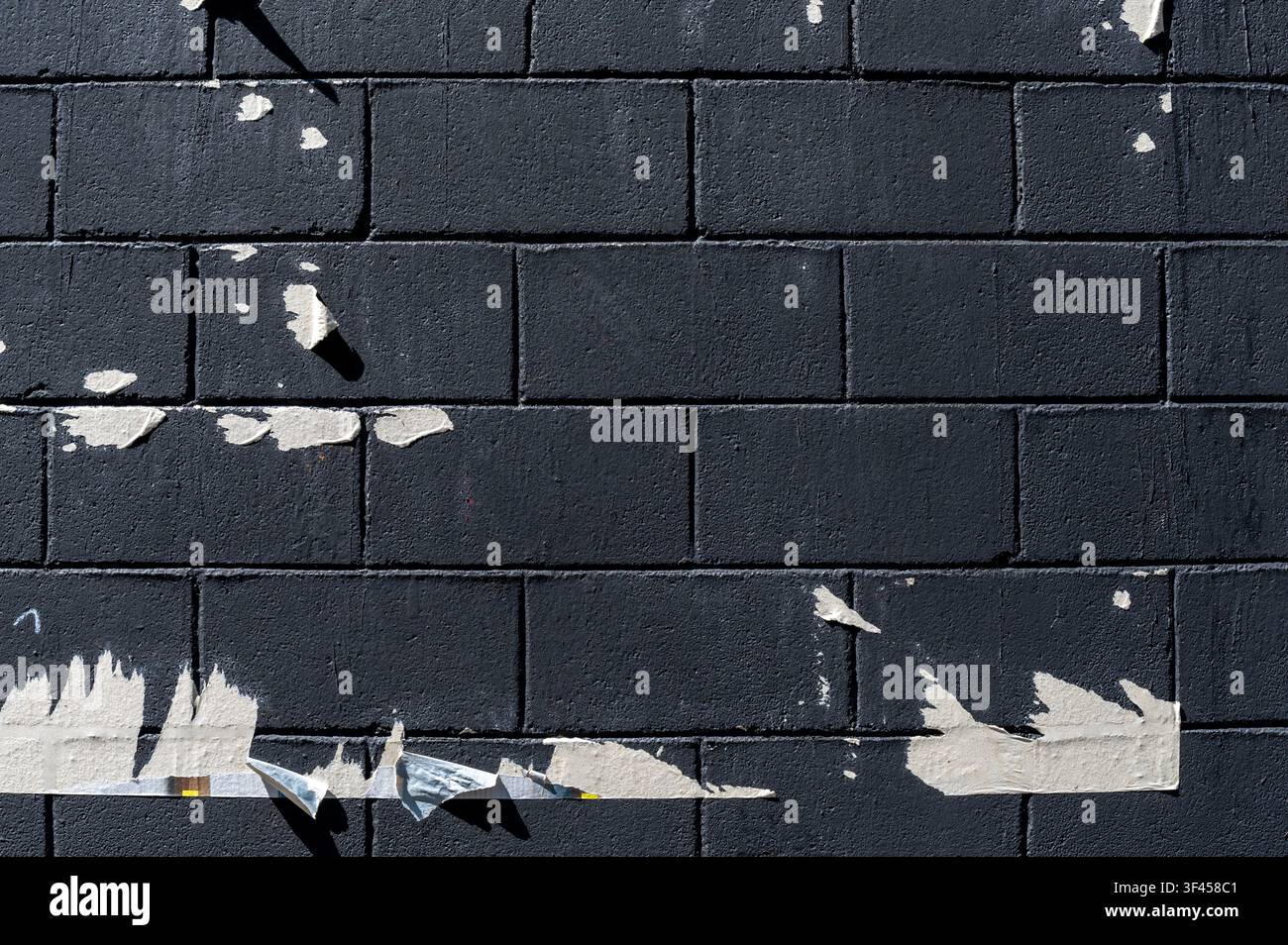 Mur de briques sombres trouvant sa texture dans des restes de papier déchirés et des ombres dures sous la lumière du soleil Banque D'Images