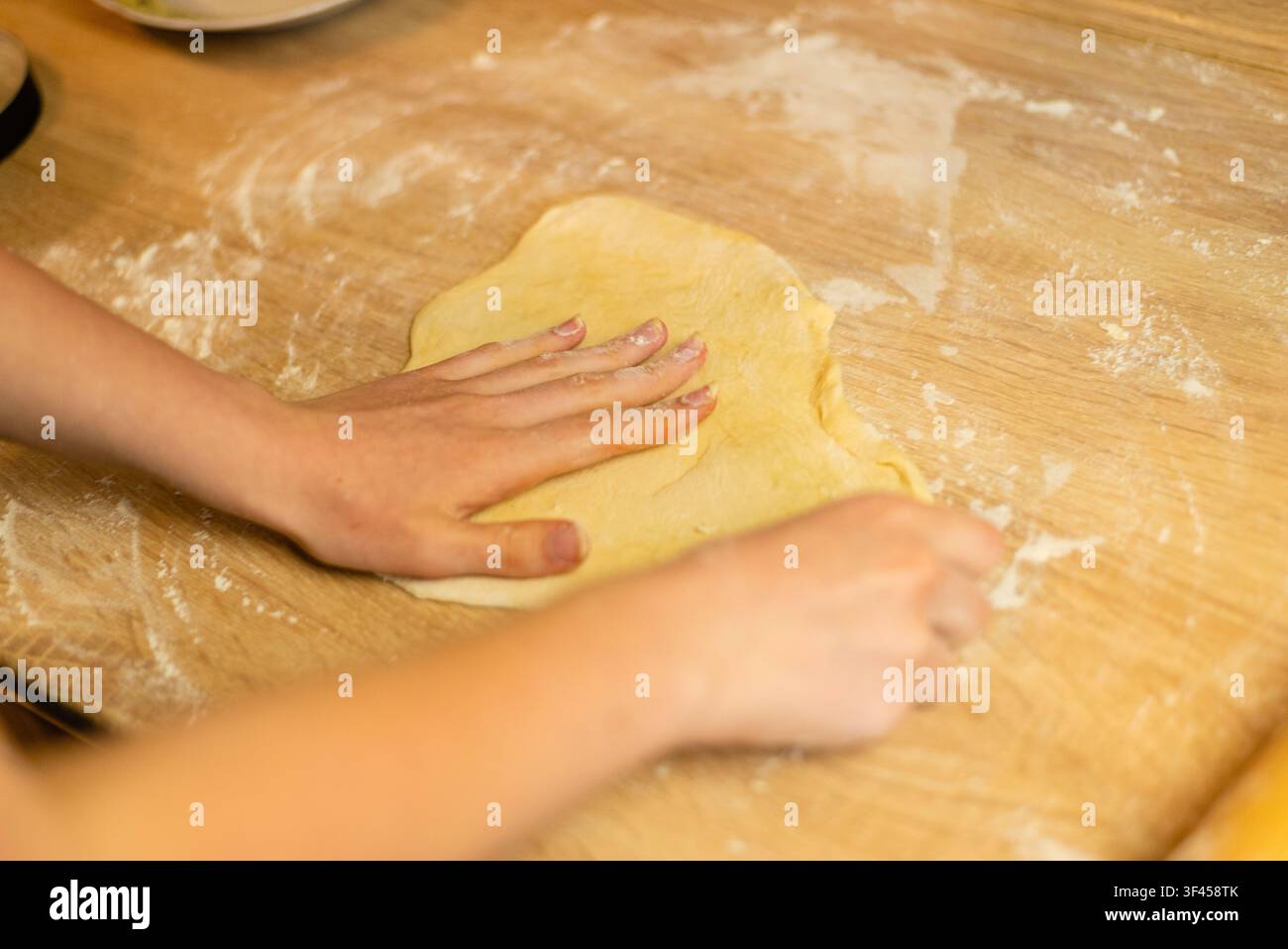 Vue rapprochée d'une personne pressant et façonnant une pièce de pâte crue sur le plan de travail de la cuisine Banque D'Images